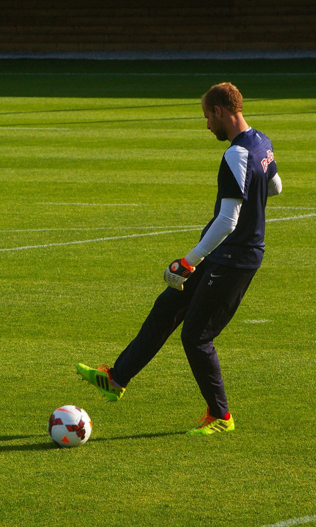 Ein Mann in einem Fußballtrikot schießt einen Ball auf einem Feld und sieht entschlossen aus.
