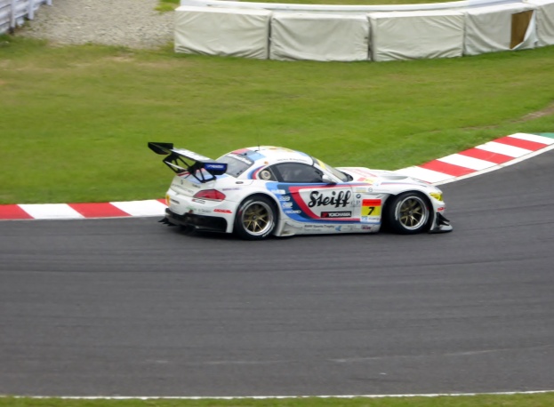 Ein Porsche 911 GT3 RSR Rennauto auf einer Rennstrecke, umgeben von grünem Gras und einem Zaun, mit Text und Zahlen, die seine Teilnahme an den 24 Stunden von Le Mans anzeigen.