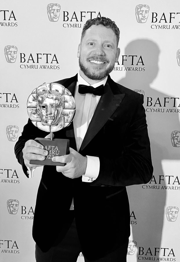 Ein Mann im Smoking mit einem BAFTA-Award, der lächelt, vor einem Hintergrundschild mit der Aufschrift "BAFTA Awards 2018."