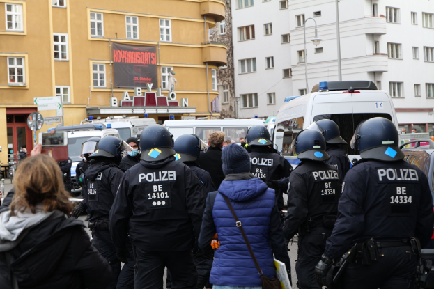 Polizeibeamte in Uniform vor einer Menge von Menschen mit Helmen und Jacken während einer Demonstration in Berlin, Deutschland.