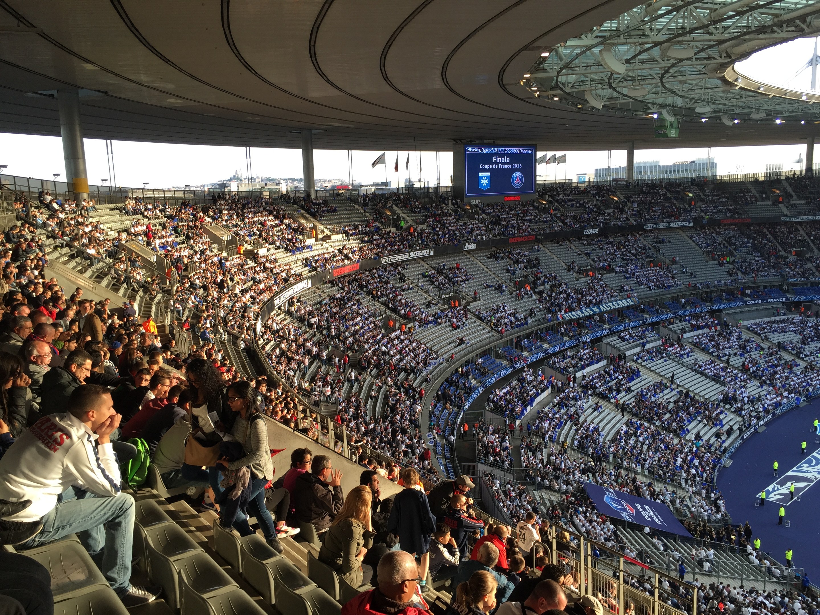 Große Menschenmenge in einem Stadion bei einem Fußballspiel mit einer Bühne, Fahnen, Stangen und einem Bildschirm im Hintergrund