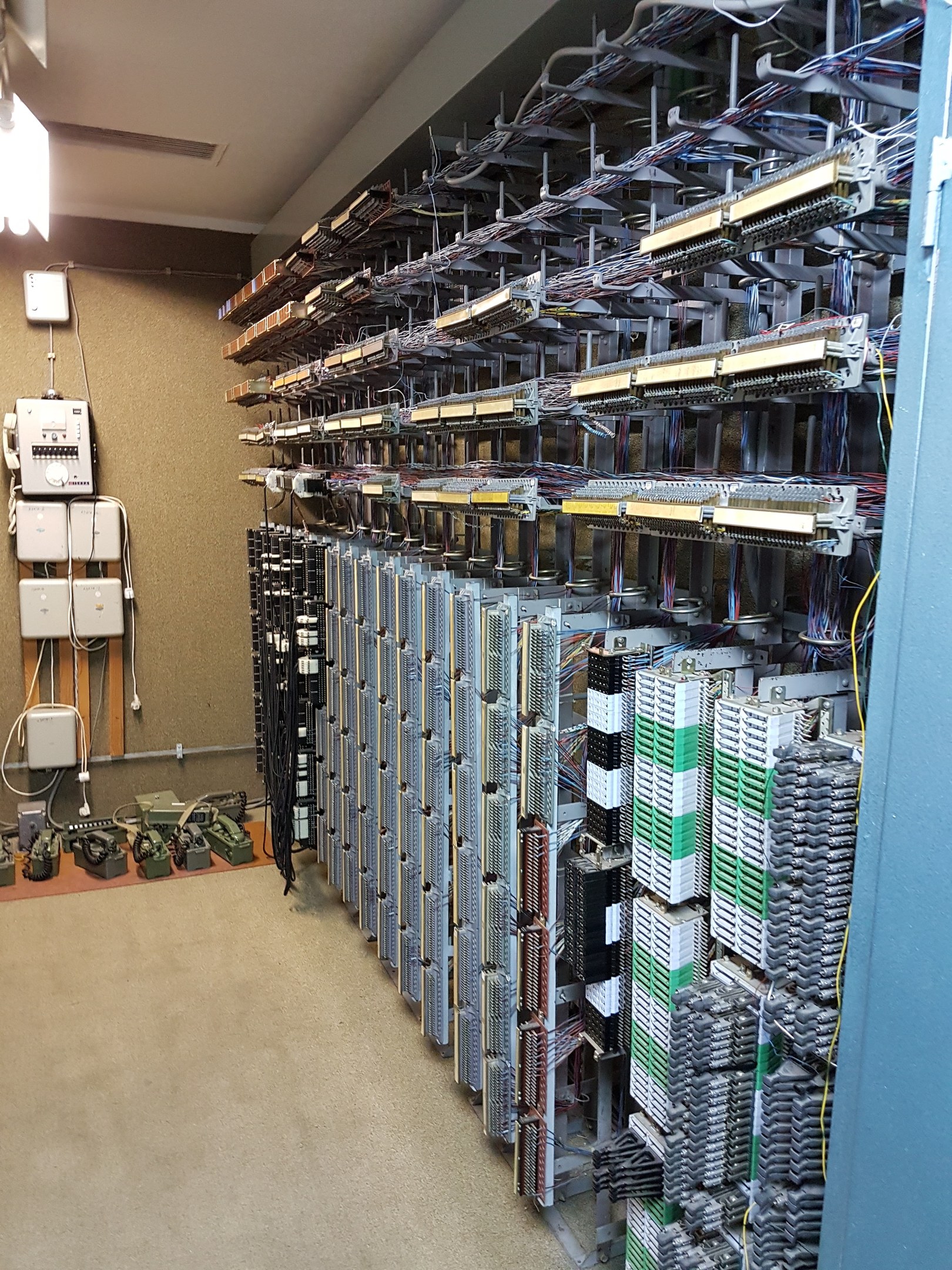 Großer Raum mit zahlreichen Kabeln und elektronischen Geräten auf dem Boden, darunter Server und Kabel, was auf ein Rechenzentrum mit einer Wand auf der linken Seite hinweist.