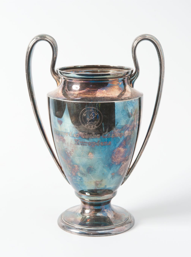 Der UEFA-Champions-League-Pokal, ein stählerner Becher mit zwei Griffen, in Blau und Silber gehalten, mit der Inschrift "UEFA Champions League" auf einem weißen Hintergrund.