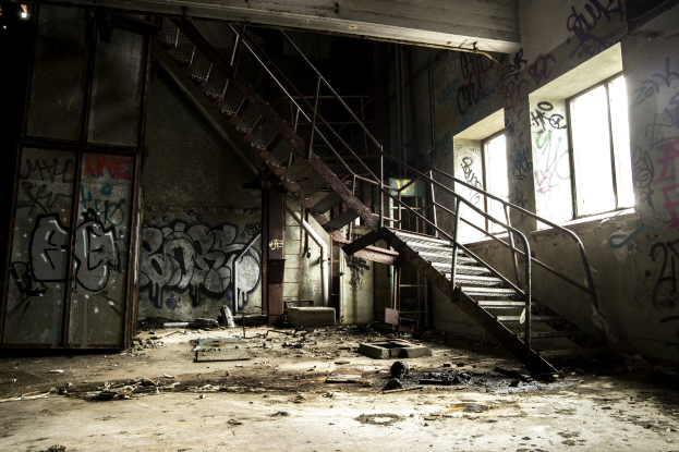 Verlassenes Gebäude mit graffiti-bedeckten Wänden, Treppe mit Geländern, die zum zweiten Stock führen, Fenster auf der rechten Seite, eine Tür auf der linken Seite und verstreute Gegenstände auf dem Boden.