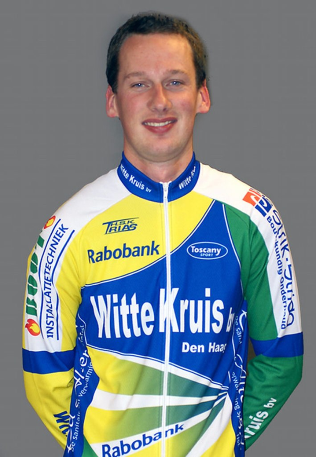 Ein männlicher Athlet posiert für ein Foto, trägt ein Hemd mit mehreren Sponsorenlogos.