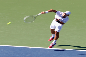 Eine Person in einem weißen Kleid springt in die Luft und hält einen Tennis-Schläger, vor sich einen Tennisball.