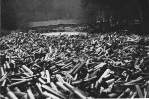 Ein Schwarz-Weiß-Foto von einem großen Haufen Patronen im Vordergrund, mit einer Hütte und Bäumen im Hintergrund und dem Text "Zweiter Weltkrieg" unten.