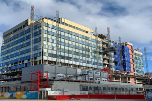 Großes Gebäude im Bau in einer Stadt mit Glasfenstern, Metallrahmen, einer Treppe, einem Zaun, einem Schild, Polen, einem Straßenpfosten, Bäumen und einem bewölkten Himmel.