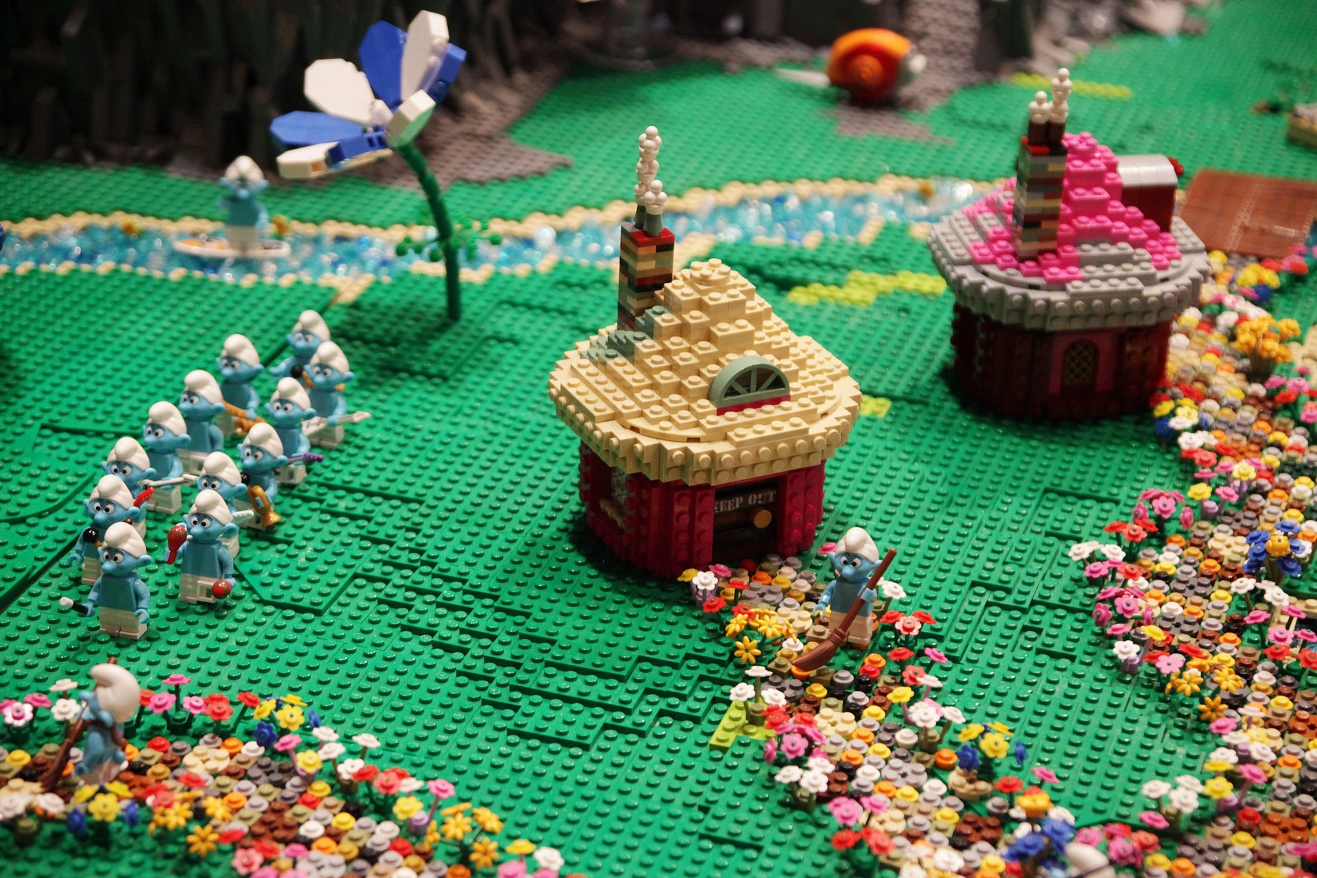 Ein Lego-Modell einer Kleinstadt mit bunten Blumen, Häusern, Pflanzen und verschiedenen Spielzeugen vor einem sanft unscharfen Hintergrund.