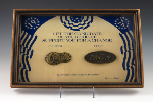 Ein gerahmtes Poster mit der Aufschrift "Lass den Kandidaten deiner Wahl dich für einen Wandel unterstützen" und Ford- und Carter-Logos.