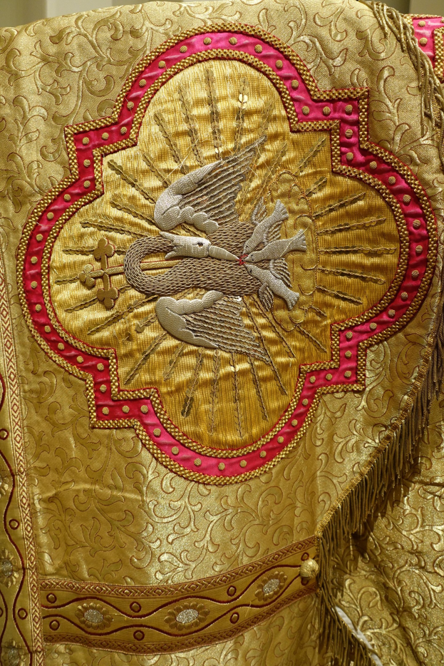 Nahaufnahme eines Priestergewandes mit aufwendiger goldener und roter Stickerei vor einer Wand im Hintergrund.