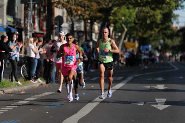 Gruppe von Menschen, die einen Marathon in einer Stadtstraße mit Zuschauern, Bäumen, Gebäuden und einem Fahrrad im Hintergrund laufen