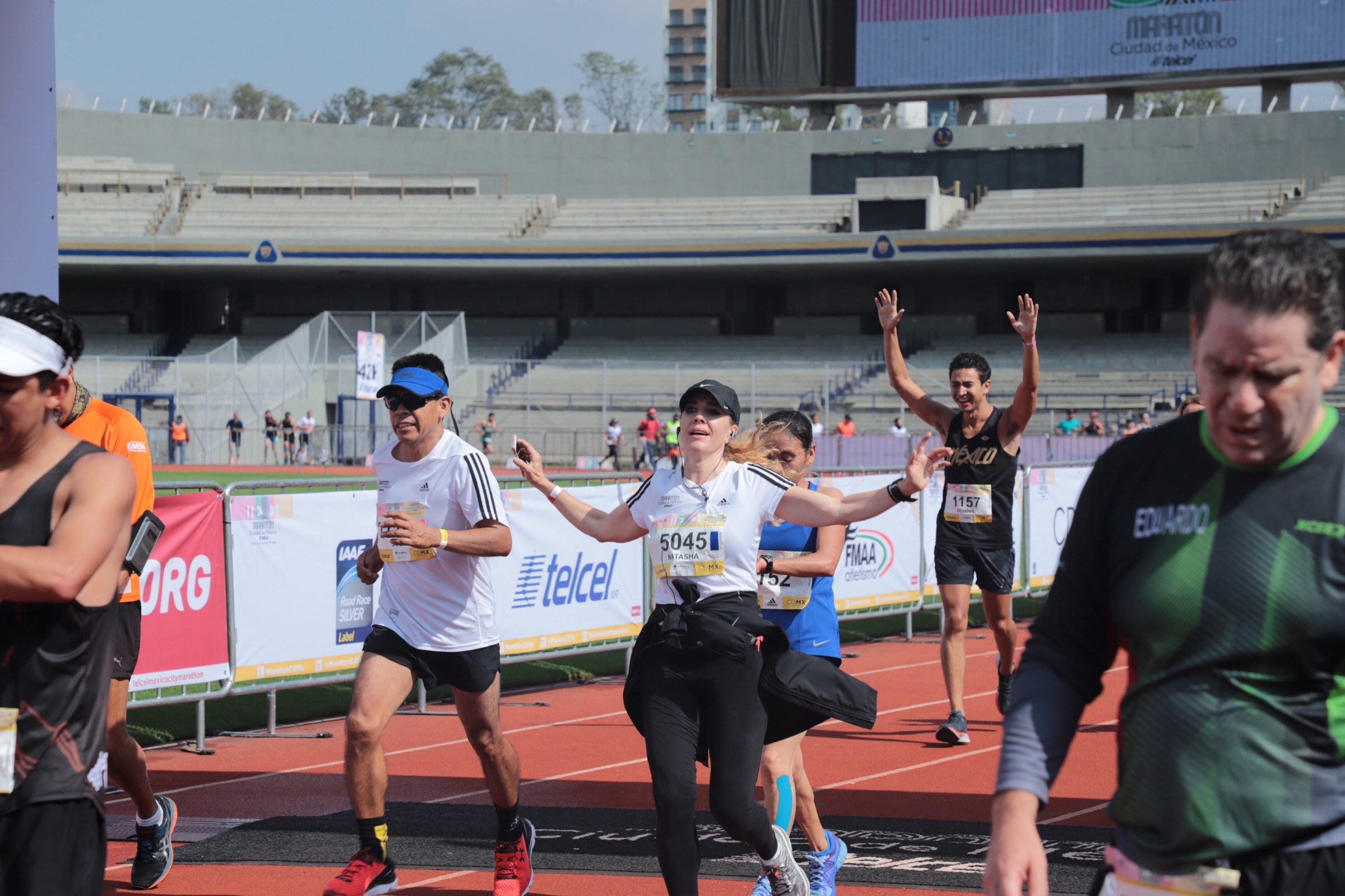 Gruppe von Menschen, die auf einer Outdoor-Sportanlage laufen; einige tragen Turnschuhe und Hüte.