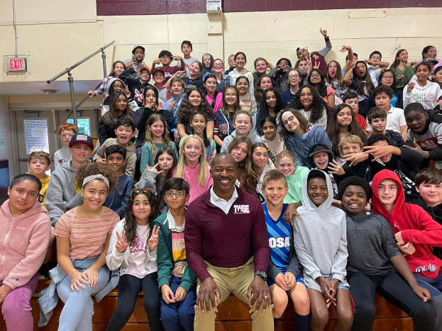 Gruppe von Schülern, die in einer Turnhalle für ein Foto posieren, wobei einige auf der Treppe sitzen und andere stehen, eine Tür und ein Ausgangsschild auf der linken Seite sichtbar