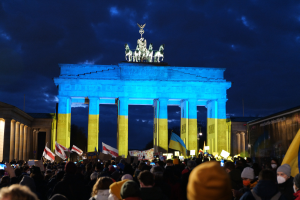 Eine Menschenmenge steht vor dem Brandenburgertor in Berlin und hält Fahnen und Schilder, auf denen ein Banner auf der rechten Seite des Bildes zu sehen ist.