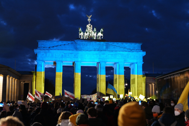 Eine Menschenmenge steht vor dem Brandenburgertor in Berlin und hält Fahnen und Schilder, auf denen ein Banner auf der rechten Seite des Bildes zu sehen ist.