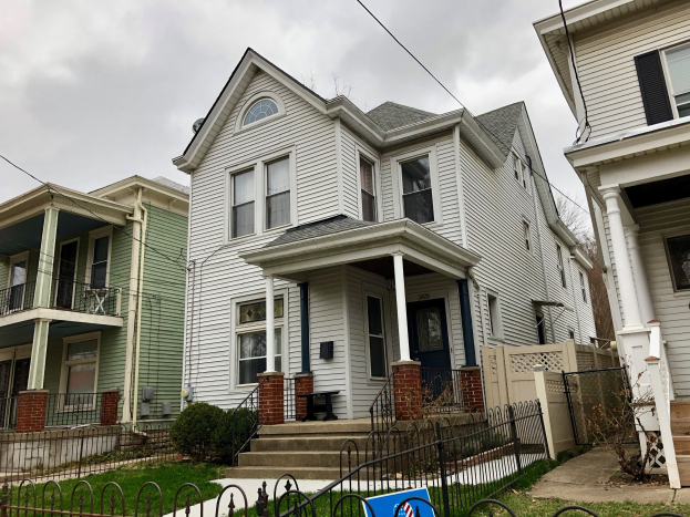 Reihe von Häusern mit Fenstern, Türen, Säulen, Geländern, Stufen und Dächern, umgeben von einem Metallzaun, Gras, Pflanzen, Bäumen und einem bewölkten Himmel, mit einem Mietschild unten, das die Adresse 5901 S Elmwood Ave, Chicago 60618 angibt.