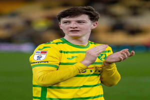 Ein junger Mann in einem gelb-grünen T-Shirt steht auf einem Fußballfeld und klatscht in die Hände, während der Hintergrund unscharf ist.