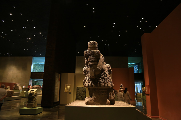 Gruppe von Menschen in einem Museum, die Skulpturen auf Sockeln unter Deckenbeleuchtung betrachten, mit sichtbaren Wänden im Hintergrund.