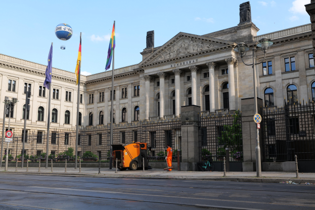 Großes modernes Gebäude mit vielen Fenstern, als Bundestag in Berlin, Deutschland identifiziert, umgeben von Straßeninfrastruktur, Fußgängern und Fahrzeugen unter einem bewölkten Himmel.