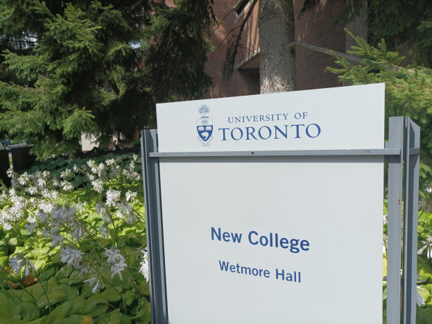 Außenansicht des neuen Colleges der University of Toronto an Wetmore Hall, mit einem Schild vor dem Gebäude, umgeben von grünem Gras, bunten Blumen, hohen Bäumen und einem klaren blauen Himmel.