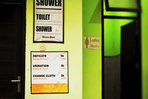 Ein Badezimmer mit einer Tür auf der linken Seite und einer grünen Wand auf der rechten Seite, das zwei Plakate zeigt: eines mit der Aufschrift "Dusche" und das andere mit der Aufschrift "Toilette".