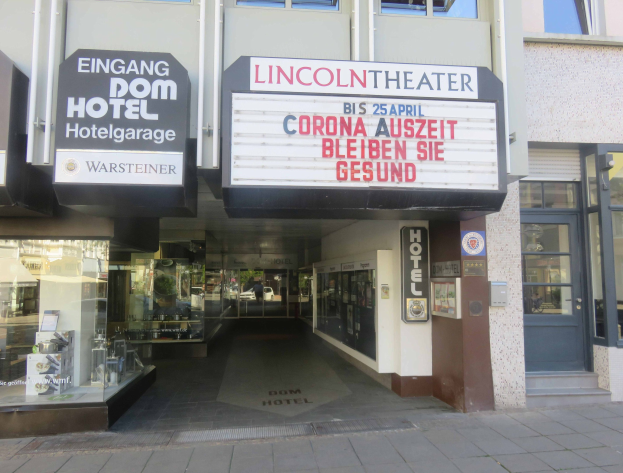 Außenansicht des Lincoln Theaters in Berlin, Deutschland, mit Glasfenstern, Türen und einer Texttafel, sowie einem Eindruck einer belebten Innenstadtlandschaft durch die Fenster