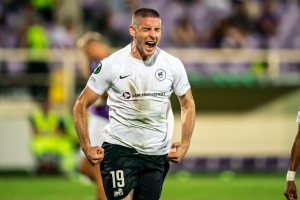 Ein Mann in einem weißen Hemd und schwarzen Shorts läuft auf einem Fußballfeld, umgeben von einer Gruppe von Menschen, die ein Tor feiern, während eines Spiels zwischen Leeds United und Melbourne Victory.