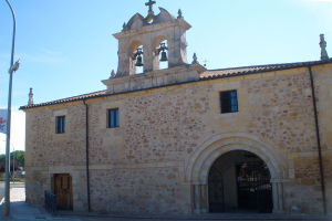Ein altes Steingebäude mit einem zentralen Uhrenturm, umgeben von Straßenmasten, Lampen, Gittern, Bäumen und einem klaren blauen Himmel, mit Fenstern, Türen und Glocken am Turm.