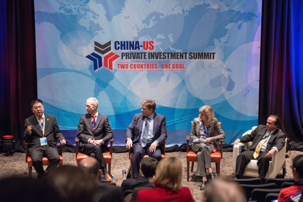 Gruppe von Menschen, die auf Stühlen sitzen und auf einen Bildschirm mit Text und einer Karte schauen, mit Vorhängen im Hintergrund, was auf einen China-US-Privatinvestment-Gipfel hindeutet.