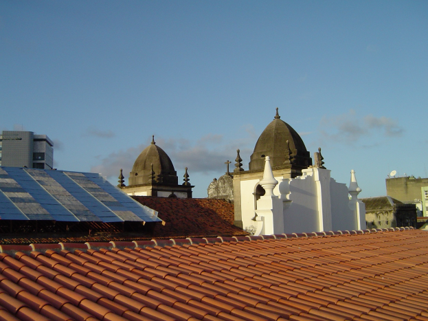 Eine Stadtansicht mit Gebäuden im Vordergrund, Solarpanelen auf einem Dach und einem blauen Himmel im Hintergrund.