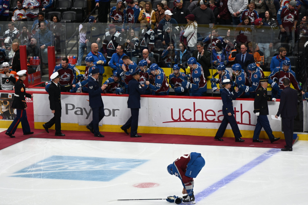 Eishockeyspieler auf dem Eis umgeben von Teamkollegen und Gegnern, mit Zuschauern im Hintergrund und Arena-Banden mit "Colorado Avalanche vs San Jose Sharks - 3/24/15 NHL Pick, Odds, and Prediction".