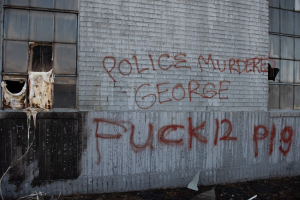 Graffiti an einer Gebäudewand lautet "Polizei ermordet George Fuck 12 P19" mit Fenstern und verstreuten Gegenständen davor.