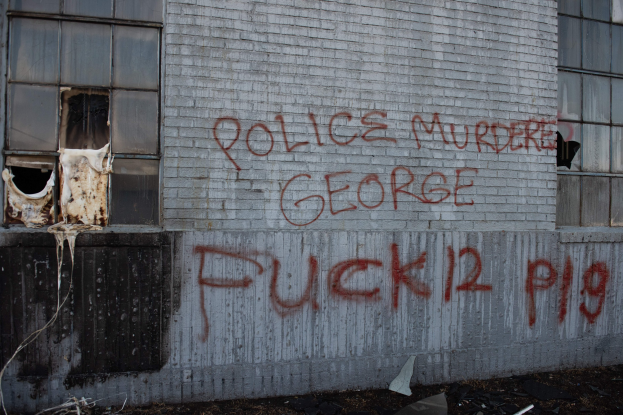 Graffiti an einer Gebäudewand lautet "Polizei ermordet George Fuck 12 P19" mit Fenstern und verstreuten Gegenständen davor.