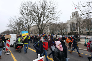 Eine große Gruppe von Menschen marschiert auf einer Straße in Washington, D.C. am 21. Januar 2020 mit Schildern und Bannern, während einige Fahrräder fahren, Schilder mit Stangen, Bäume und ein klarer blauer Himmel im Hintergrund.