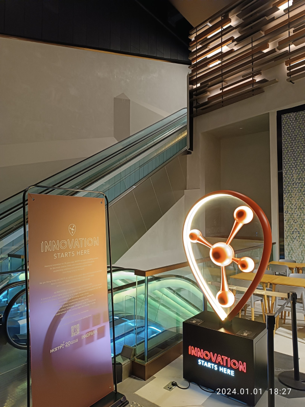 Großes Schild in der Mitte eines Gebäudes mit einer Rolltreppe im Hintergrund, Tische und Stühle auf der rechten Seite und eine Tafel mit "Innovation Starts Here" auf der linken Seite, die auf die HSTP20 Expo hinweist.