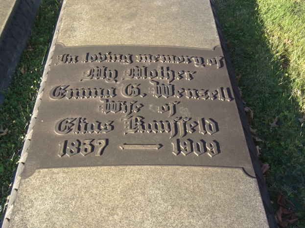 Ein Grabstein auf einem Friedhof mit der Inschrift "In liebevoller Erinnerung an meine Mutter", umgeben von Gras und welken Blättern.