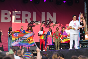Eine Gruppe von Menschen auf einer Bühne mit einem Banner, auf dem "Berlin as Fuck" steht, mit Lautsprechern, Mikrofonen und einer Menge unten, die ihre Hände hebt.