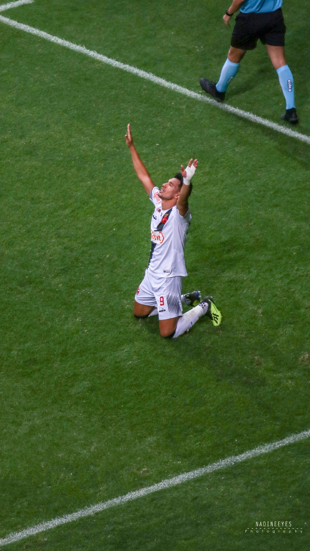 Ein Fußballspieler kniet auf dem Boden mit ausgestreckten Armen in Feierlaune, trägt eine Sportuniform und Fußballschuhe.