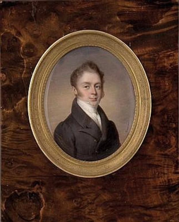 Porträt eines jungen Mannes in einem schwarzen Mantel und weißem Hemd, gerahmt in einem Foto auf einer hölzernen Oberfläche, mit ernstem Gesichtsausdruck, verschränkten Händen und ordentlich gekämmtem Haar.