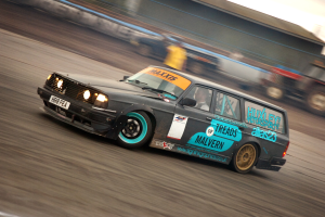 Ein Auto fährt auf einer Rennstrecke, umgeben von anderen Fahrzeugen, mit einer Person darin, der Hintergrund ist unscharf.
