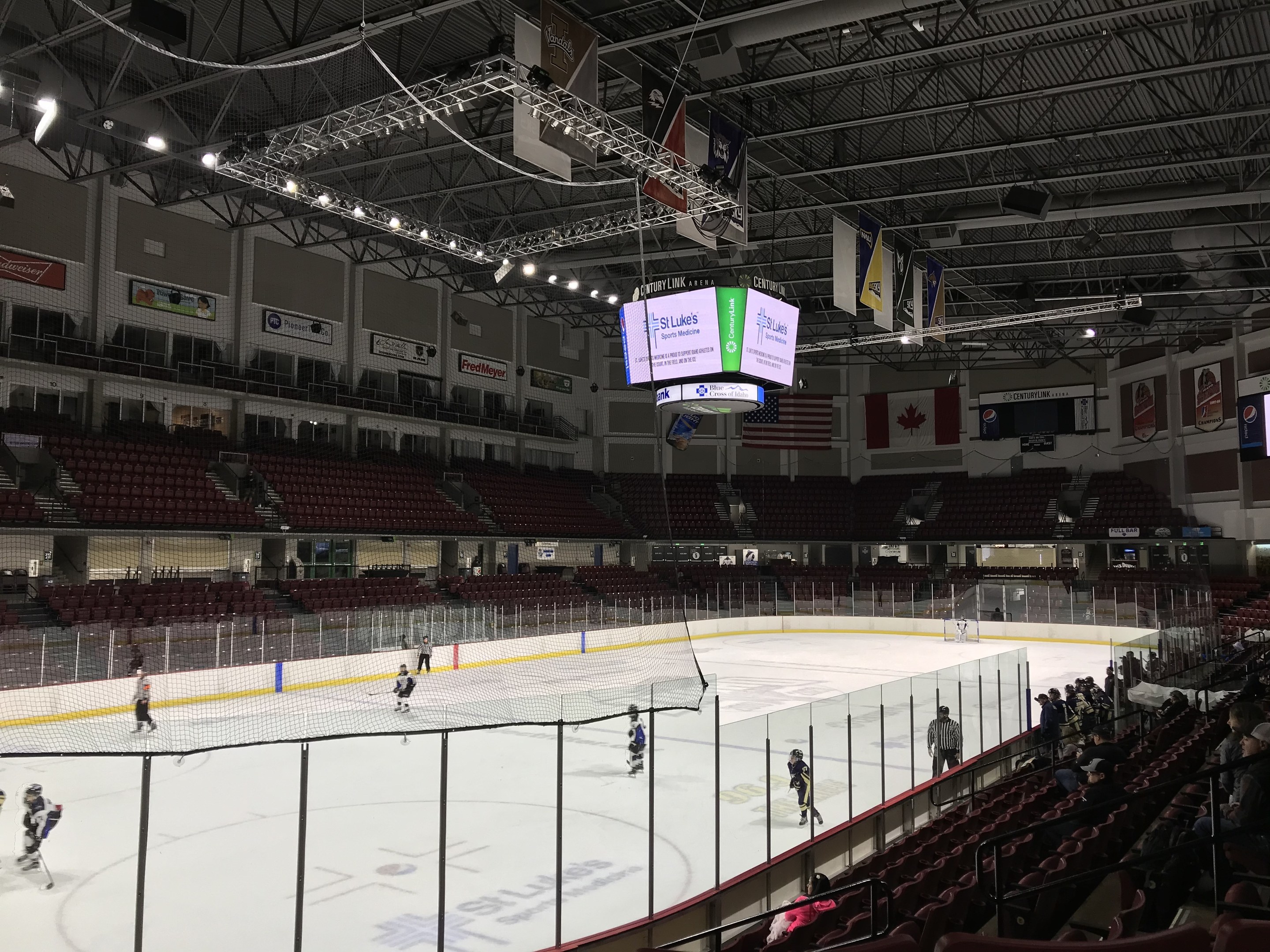 Eishockeyspiel in einer großen Arena mit Zuschauern auf beiden Seiten, mit einem zentralen Tor, Deckenbeleuchtung, Bannern und Fahnen, die für die St. Louis Blues beschriftet sind.