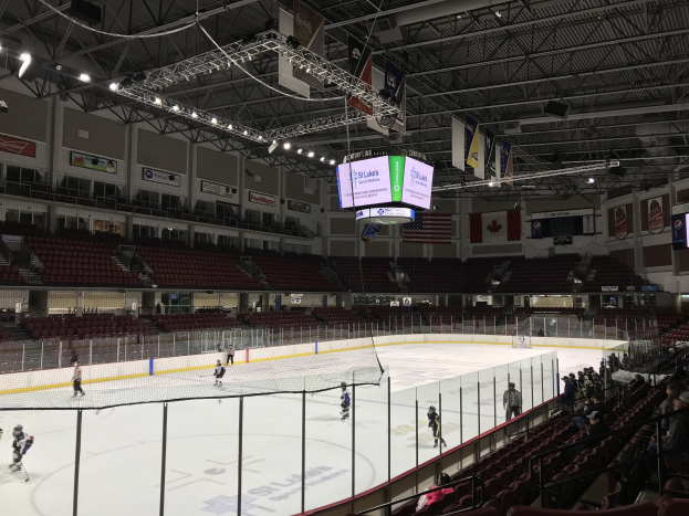 Eishockeyspiel in einer großen Arena mit Zuschauern auf beiden Seiten, mit einem zentralen Tor, Deckenbeleuchtung, Bannern und Fahnen, die für die St. Louis Blues beschriftet sind.